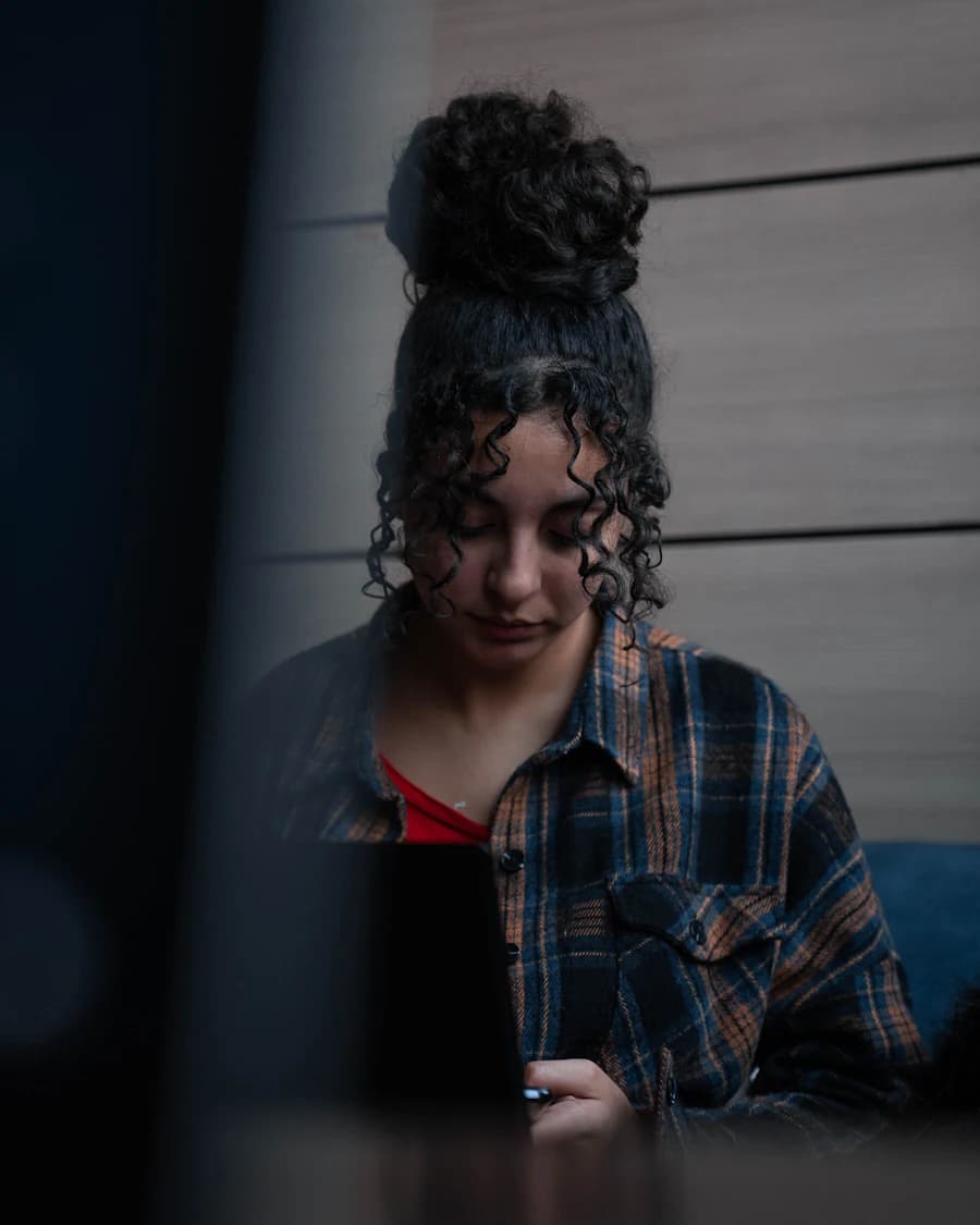 Woman with curly hair looking down at her phone in a dim room