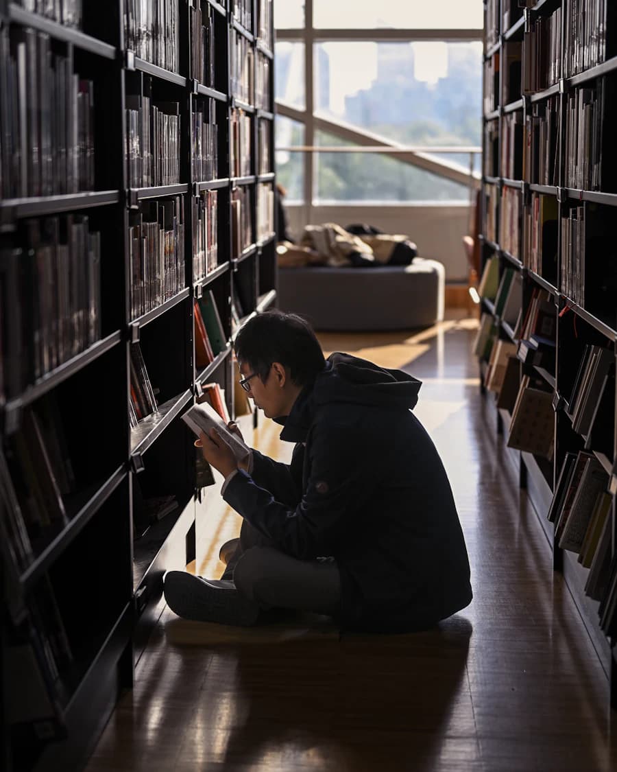 Student sitting on the floor between library shelves, reading