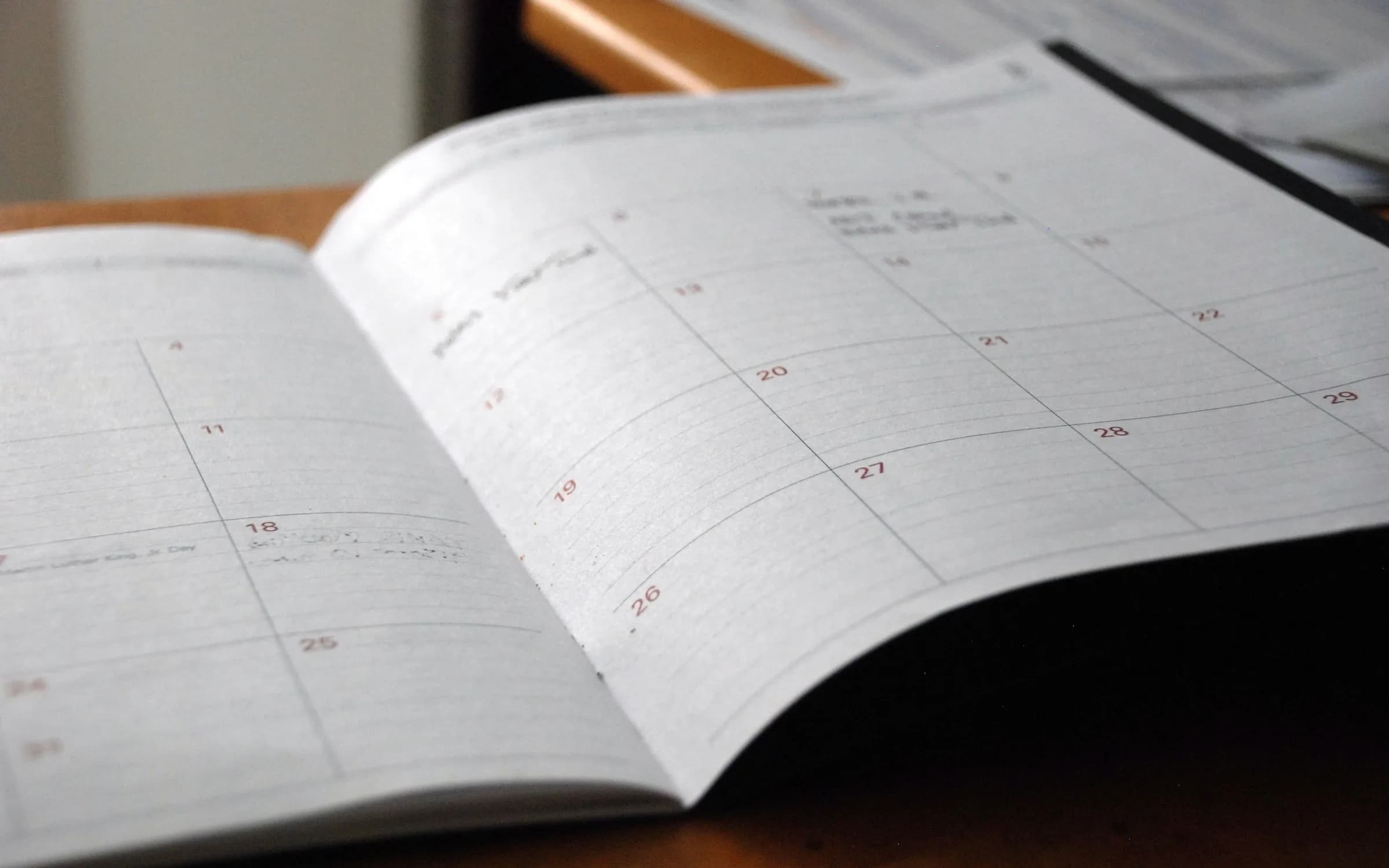 木製デスクの上に開かれた月間プランナー、いくつか手書きのメモがある