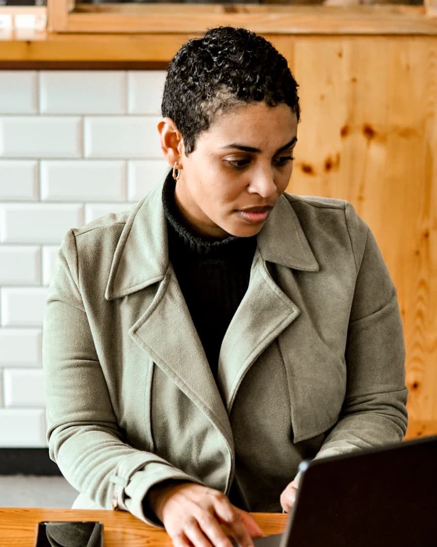 Woman in a green coat focused on her laptop at a wooden table