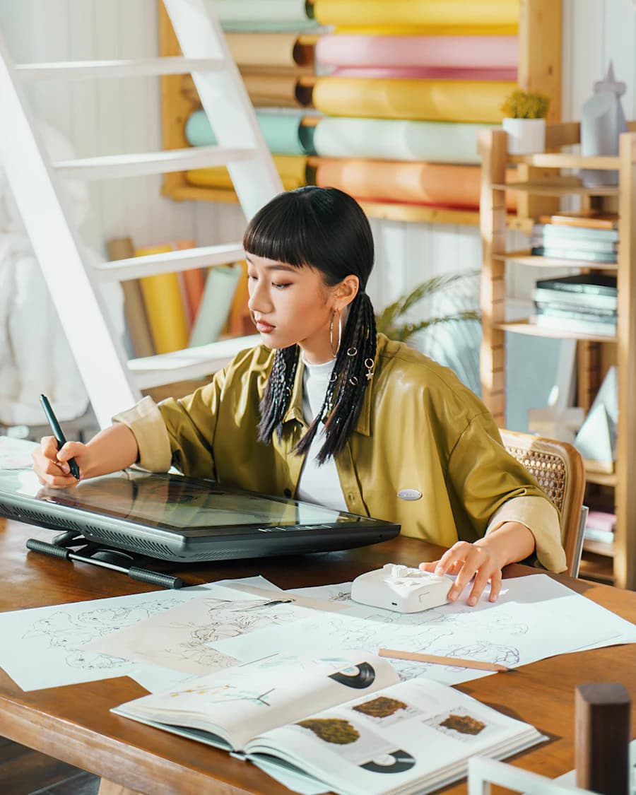 Illustrator drawing on a pen display, surrounded by sketches