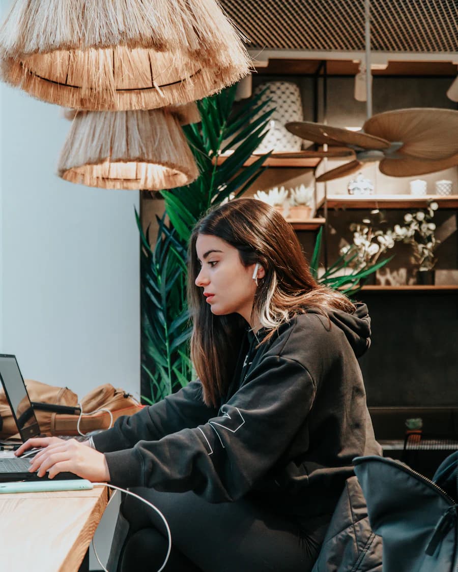 Woman in a hoodie typing on a laptop at a café counter