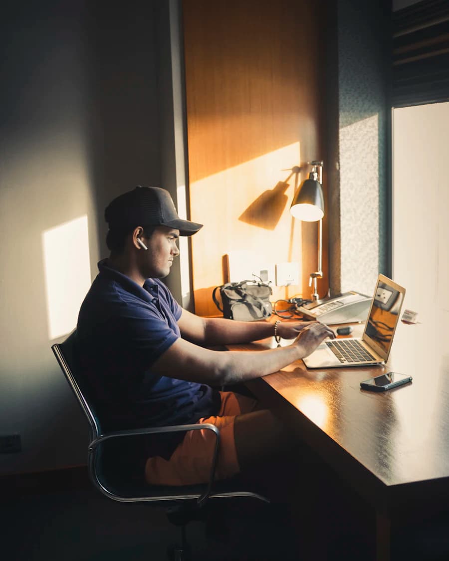 Man in a cap working on a laptop at a sunlit home desk