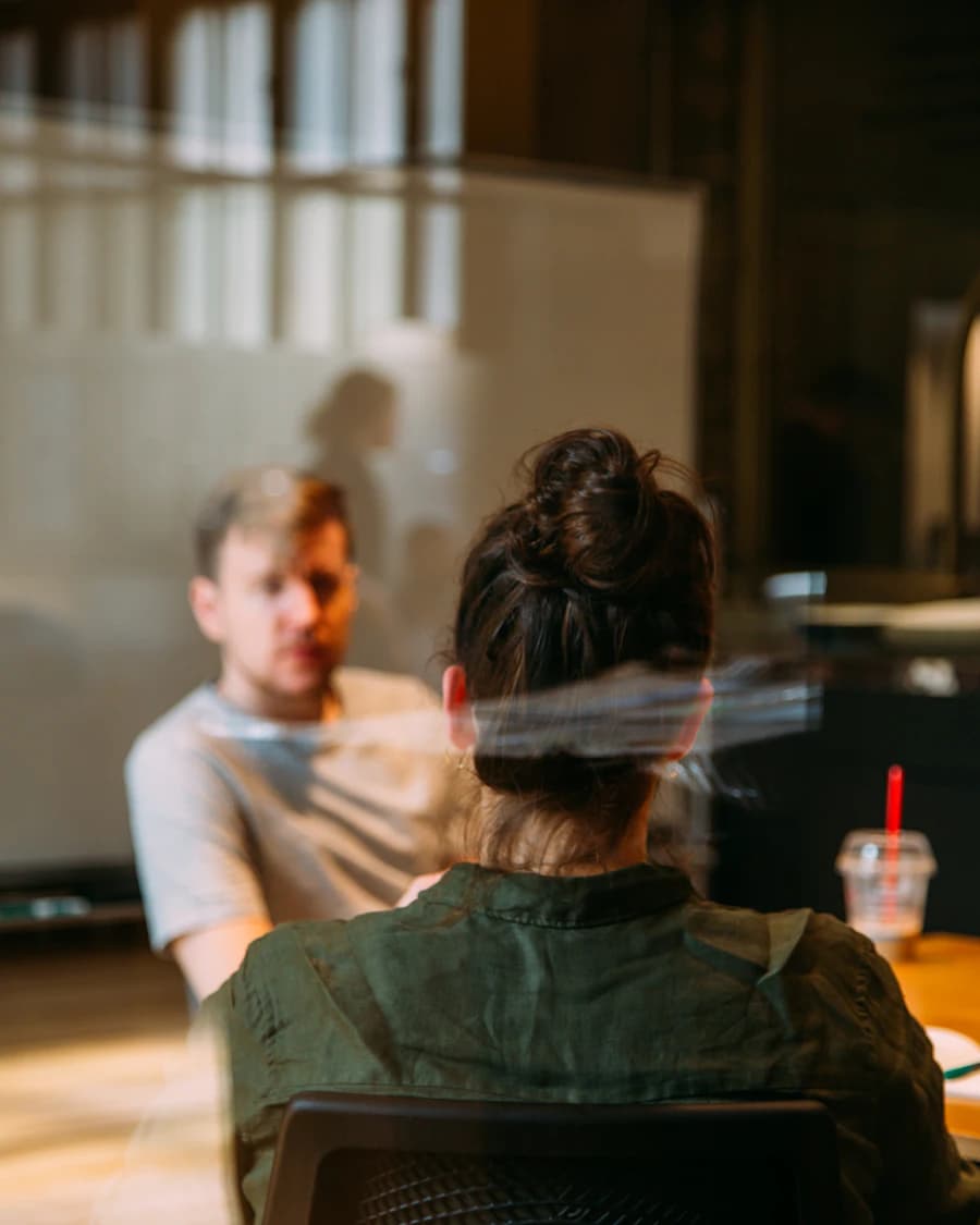 Two people in conversation at a table, seen through a glass wall