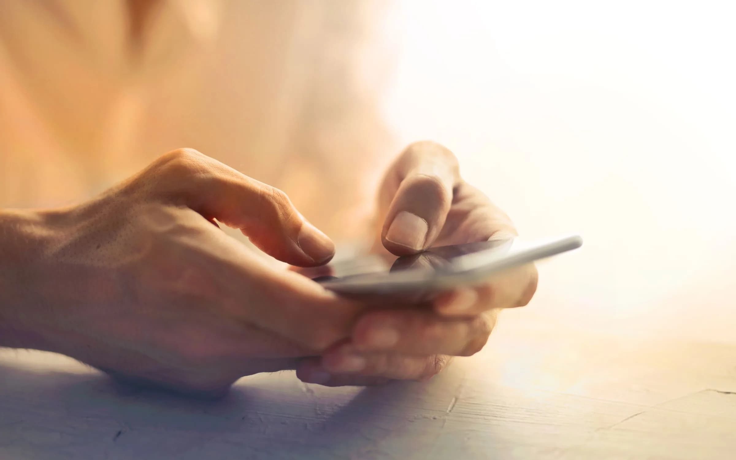 Close de duas mãos digitando em um smartphone sob a luz quente de uma janela