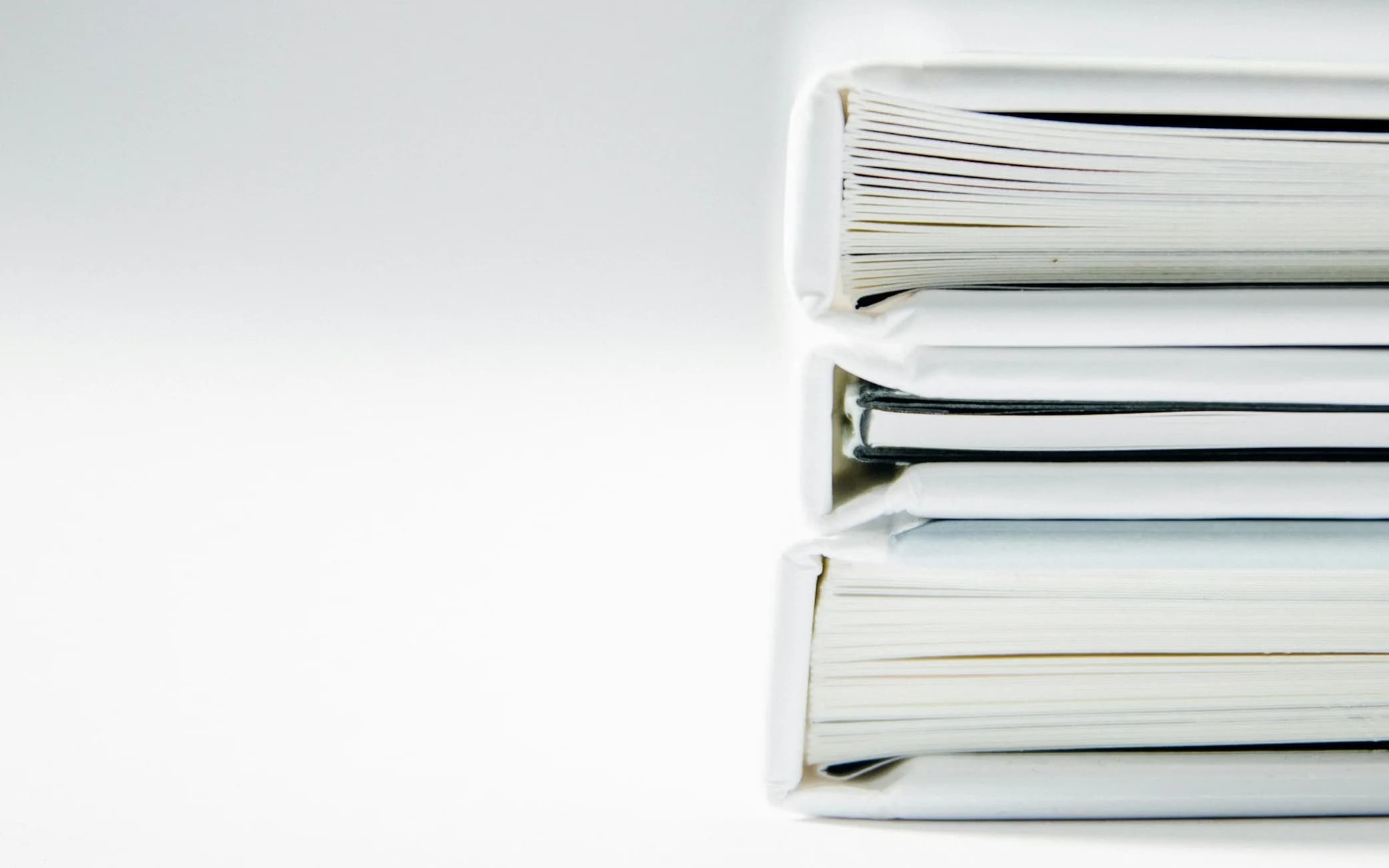 A stack of three white ring binders full of paper on a white desk