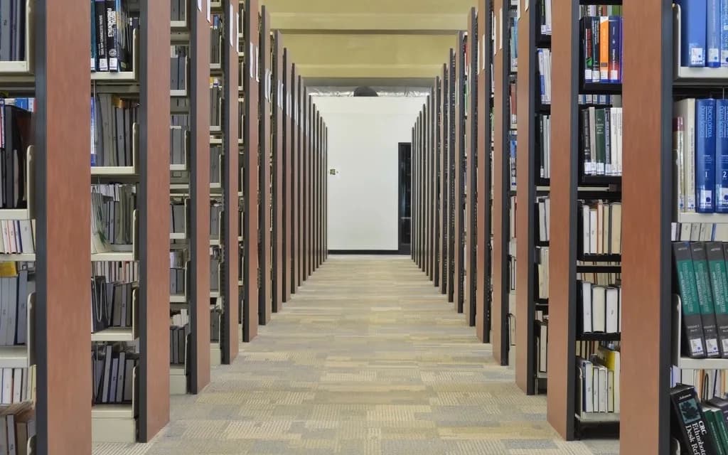 A long aisle between tall library shelves filled with books