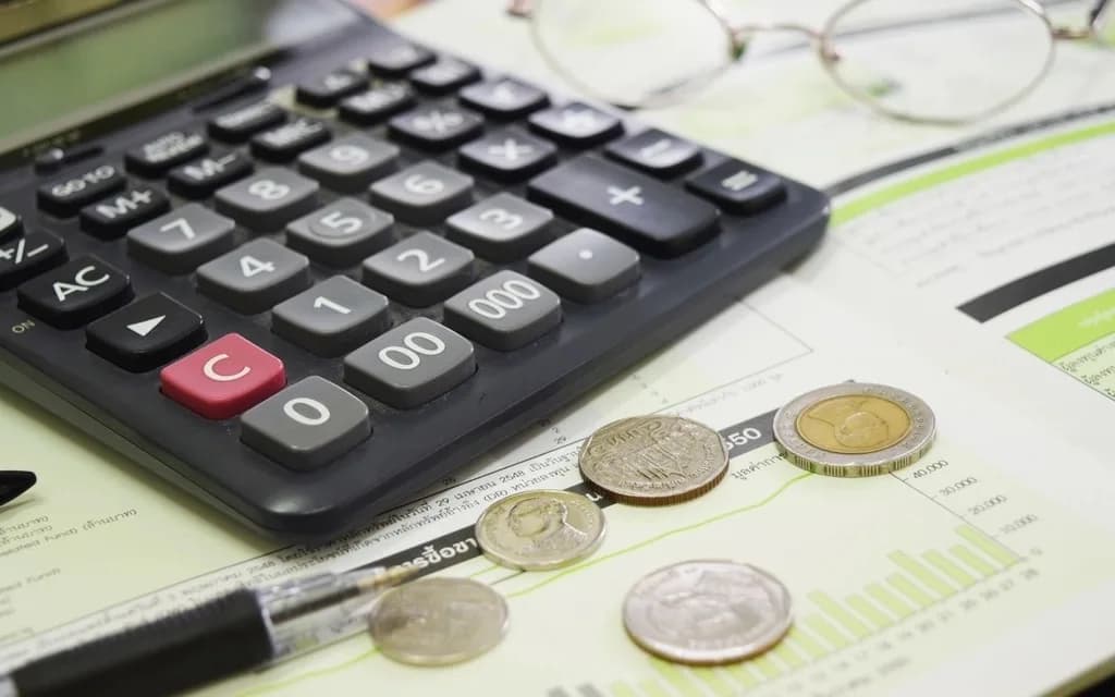 A calculator, a few coins, a pen and reading glasses on a printed budget report