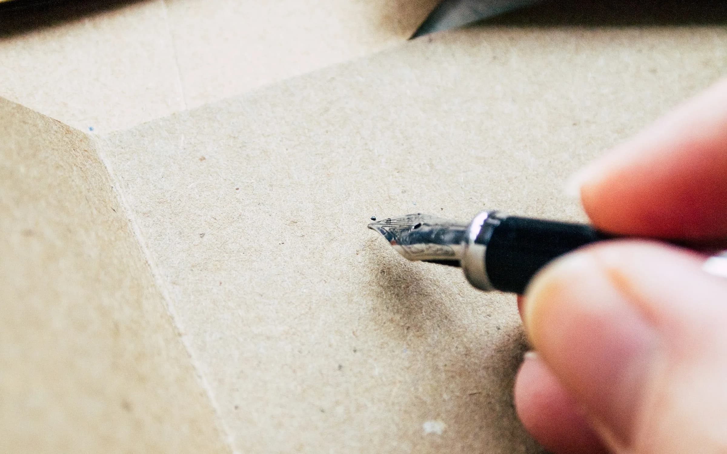 Una mano con una pluma estilográfica justo encima de una hoja de papel marrón en blanco, a punto de empezar a escribir